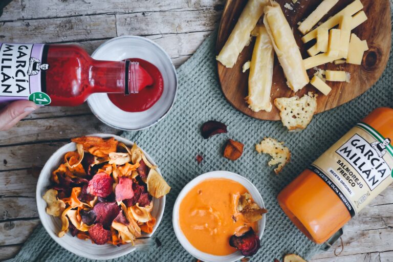 Imagen desde arriba de una mesa con chips vegetales yalgunos palillos de queso servidios con salmorejo