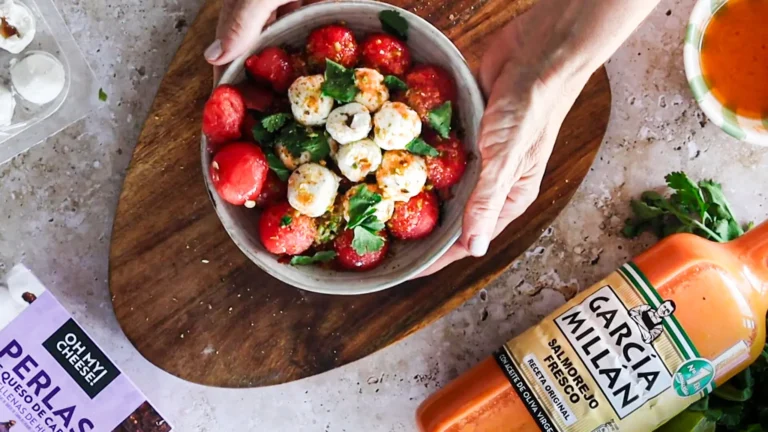 Primer plano de una ensalada fresca con bolitas de sandía, dados de tomate y aguacate, coronada con perlas de queso de cabra TGT y aliñada con el sedoso Salmorejo Tradicional García Millán